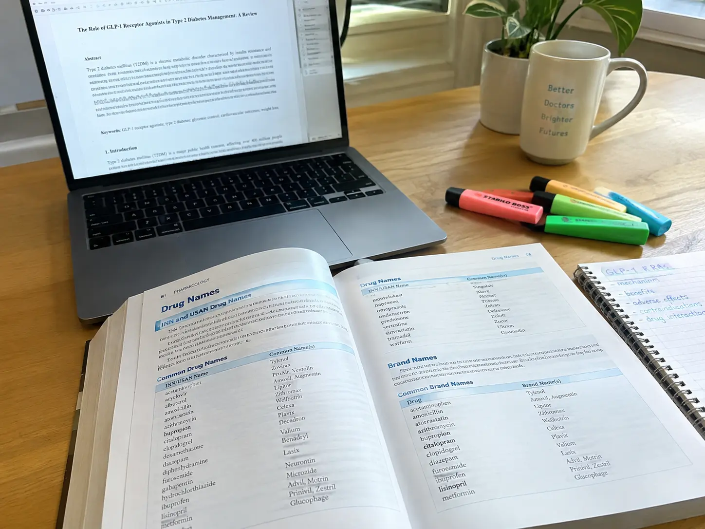 Schreibtisch mit einem aufgeschlagenen pharmakologischen Nachschlagewerk auf einer Wirkstoffnamen-Seite, Laptop mit Manuskript, farbige Textmarker